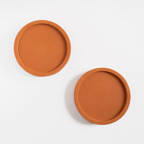 A pair of round coasters handmade using jesmonite in a terracotta colour by Klndra for Curious Makers