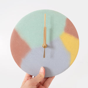 Round concrete clock in mint, yellow, brown and lilac being held to show the scale.