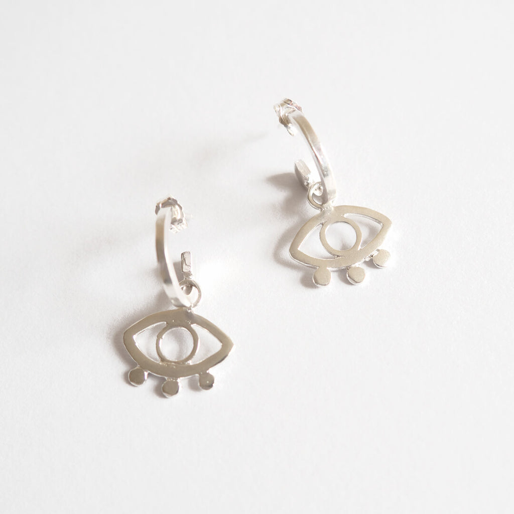 Close up of a pair of mini hoop ecosilver earrings with eye design.