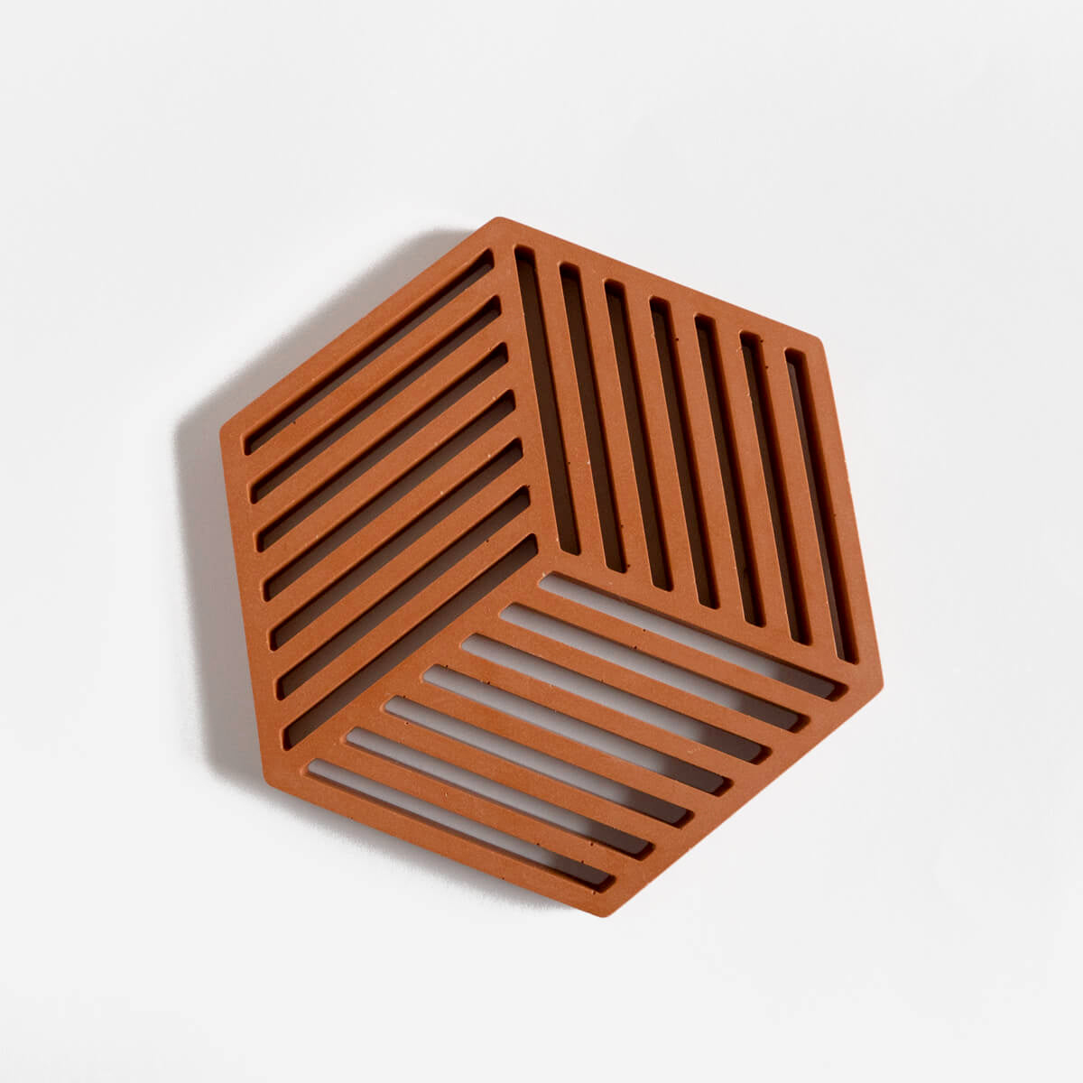 A contemporary hexagonal jesmonite trivet in a warm terracotta hue by Klndra for Curious Makers