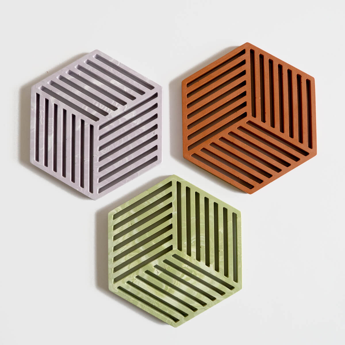 A group of 3 hexagonal jesmonite trivets in lilac, sage and terracotta handmade by Klndra for Curious Makers.