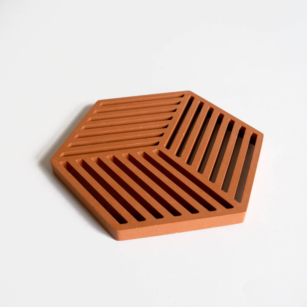 A contemporary jesmonite hexagonal trivet in a warm terracotta hue by Klndra for Curious Makers