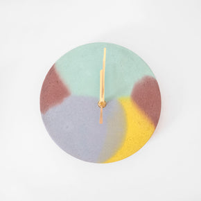 Round concrete clock with brass hands and a unique mint, yellow, brown and lilac design. By Studio Emma for Curious Makers.