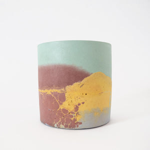 A round concrete plant pot handmade by Studio Emma for Curious Makers in a yellow and mint marbled pattern with flashes of brown and lilac.